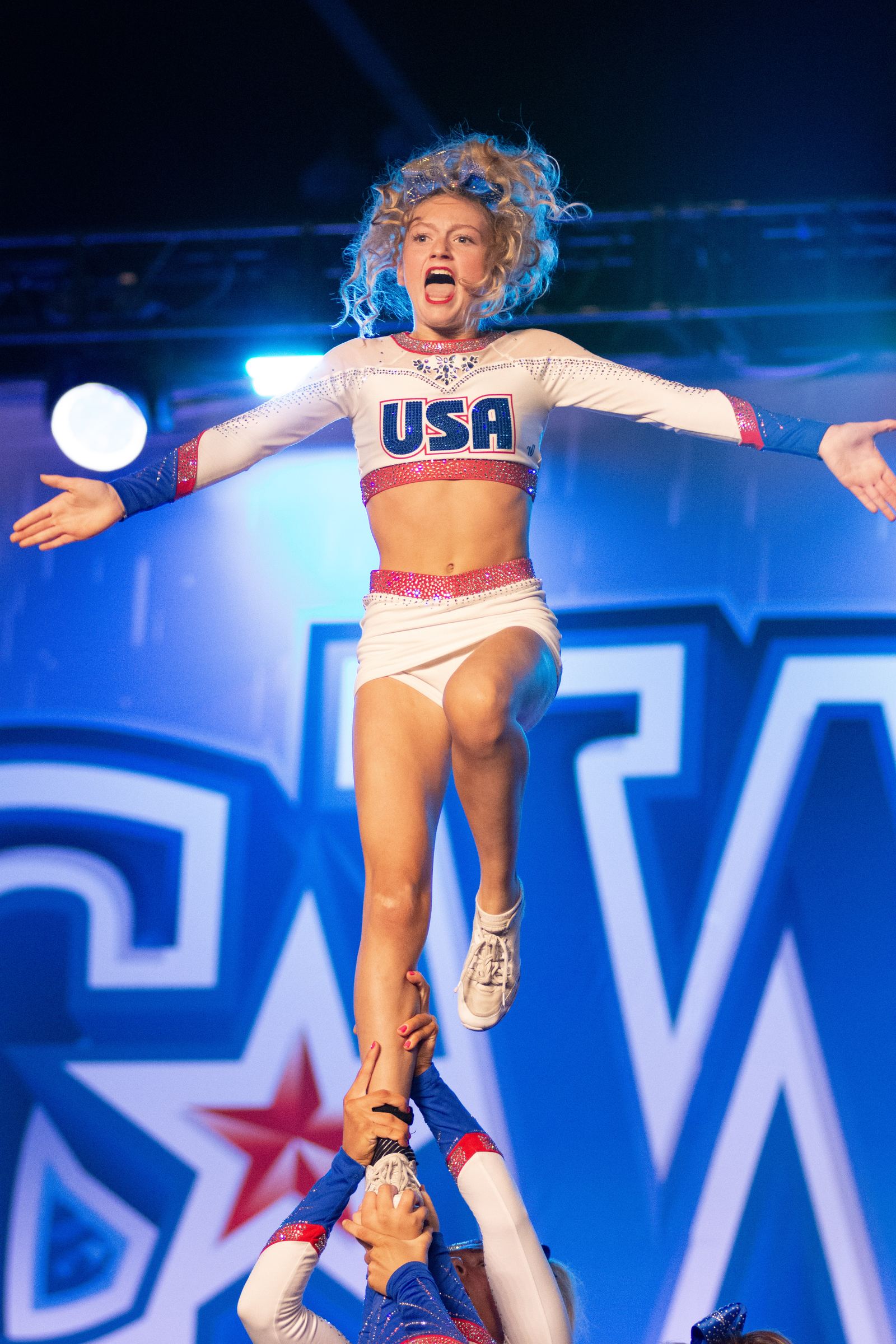 Flyer with arms spread wide above her base against a blue stage