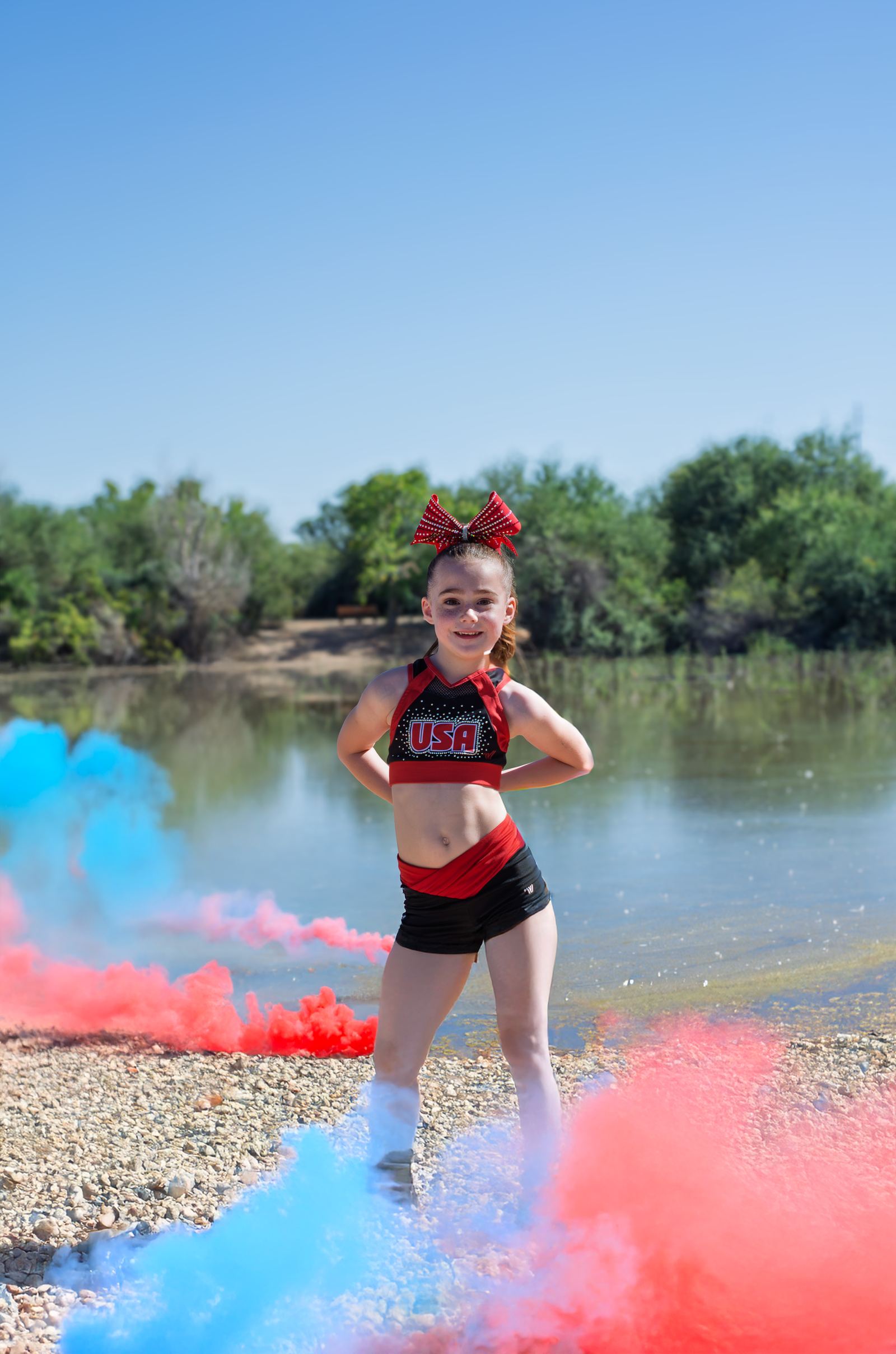 Cheer athlete posing on a lakeshore surrounded by red and blue smoke