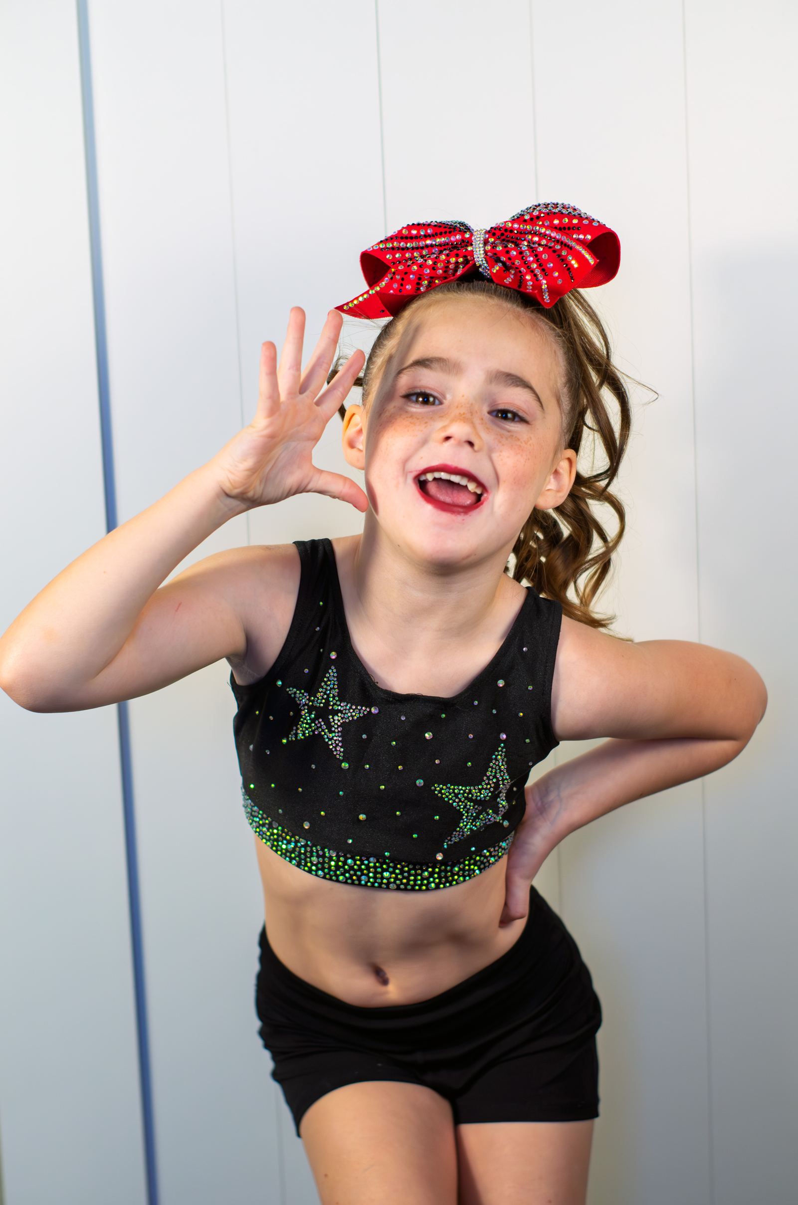 Playful studio portrait of a young cheerleader with a big red bow